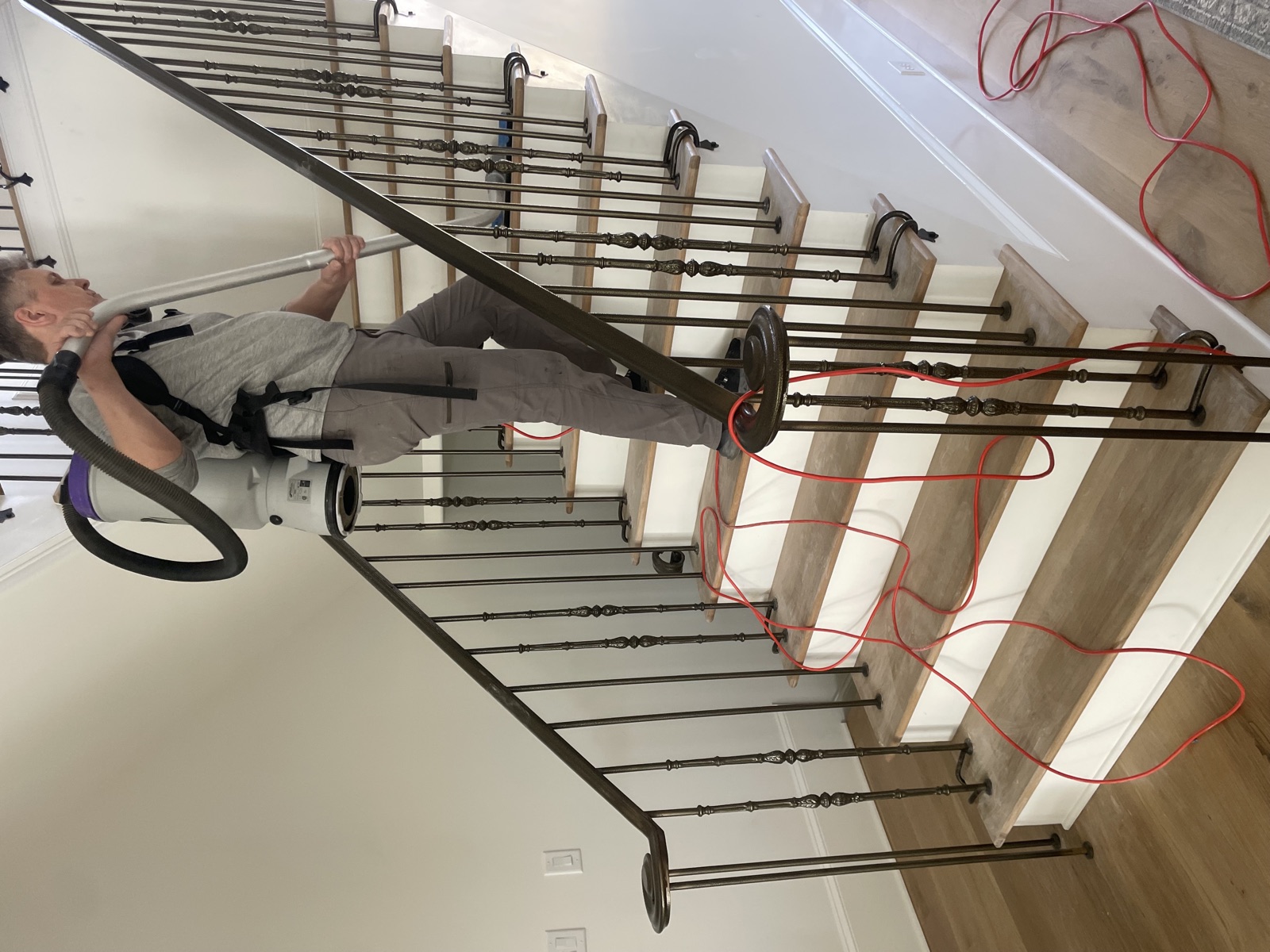 Hardwood stair treads being cleaned after installation with ornate iron baluster railing