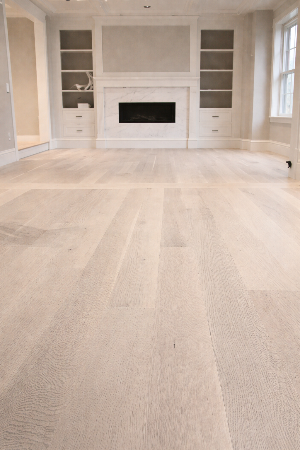 Whitewashed wide-plank hardwood in living room with marble fireplace and built-ins