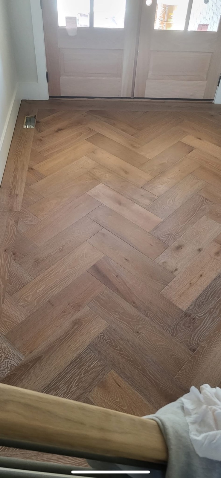 Finished herringbone pattern hardwood flooring in home entryway with double front doors
