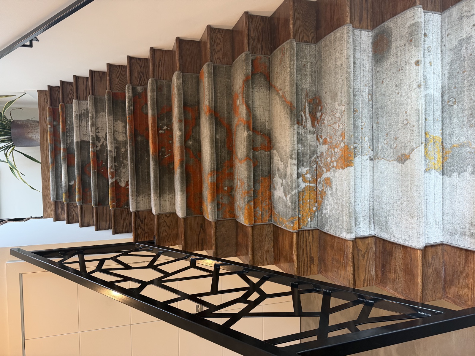 Full staircase with custom abstract carpet runners in gray and orange tones, black geometric iron railing